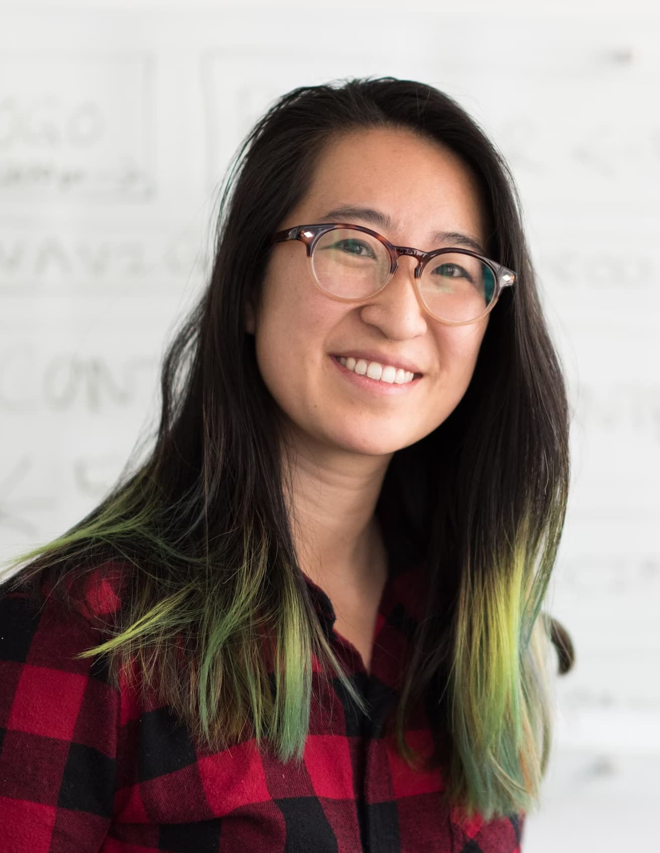 Jeanine White smiling in a red plaid shirt and tortoise shell glasses